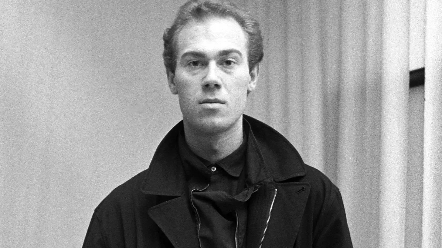 Martin Margiela as a young designer, black jacket over a black shirt, black-and-white portrait