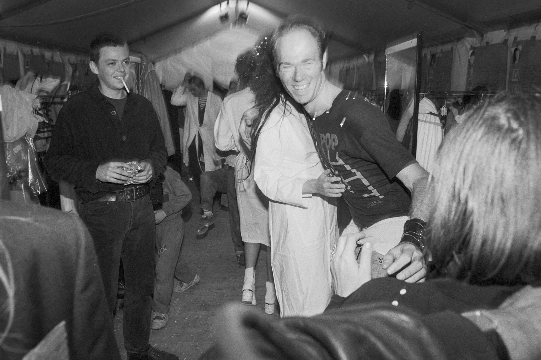 Backstage at a Maison Martin Margiela show: models in white coats among the clothes rails, black-and-white
