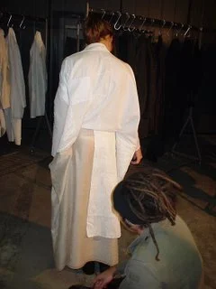 Maurizio Altieri at work, kneeling to adjust a long white garment on a client
