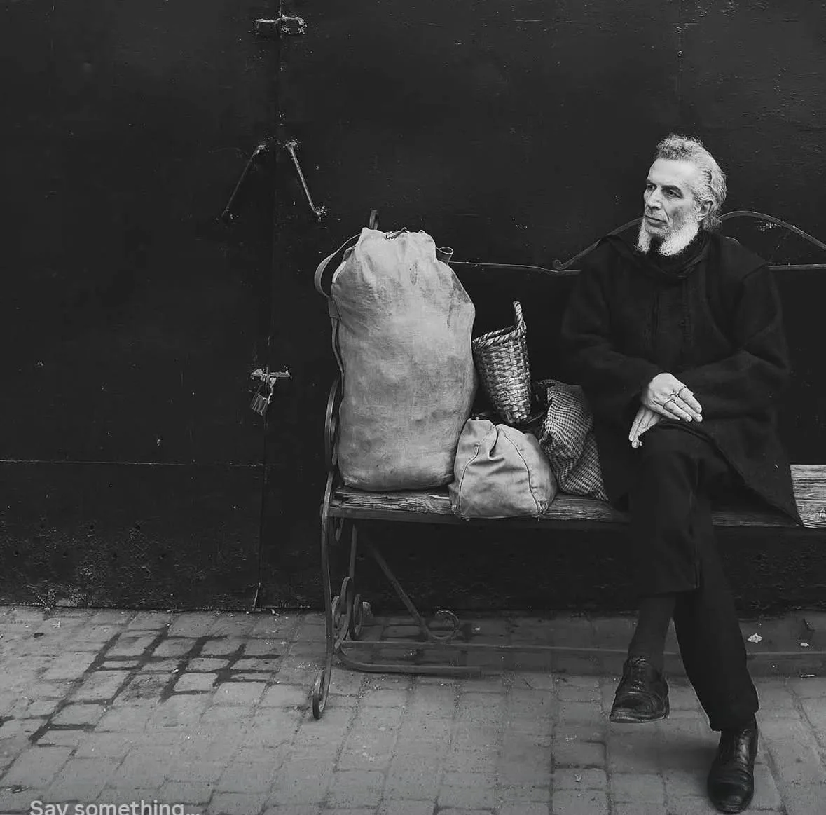 Maurizio Altieri seated on a bench beside canvas sacks, black-and-white photograph