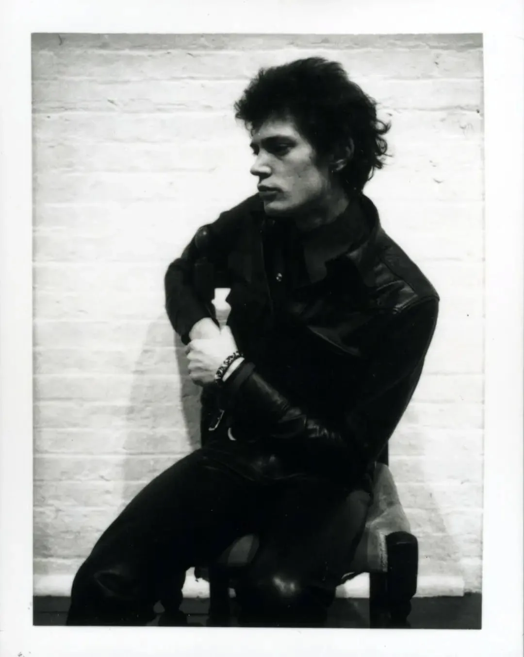 Robert Mapplethorpe in black leather, seated against a white brick wall, black-and-white Polaroid