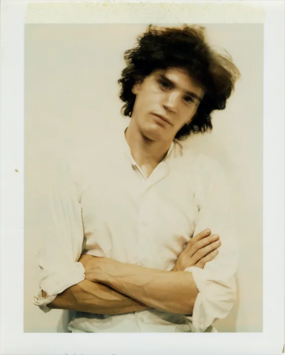 Robert Mapplethorpe in a white shirt with arms crossed, colour Polaroid